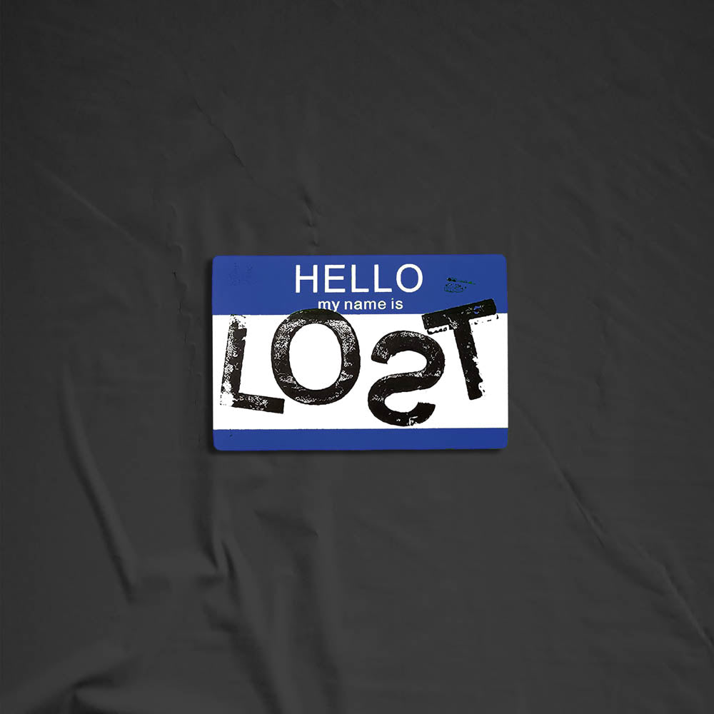 Hello my name is LOST sticker. A blue and white nametag sticker stamped with the name LOST with a backwards S. The sticker is set against a black background.