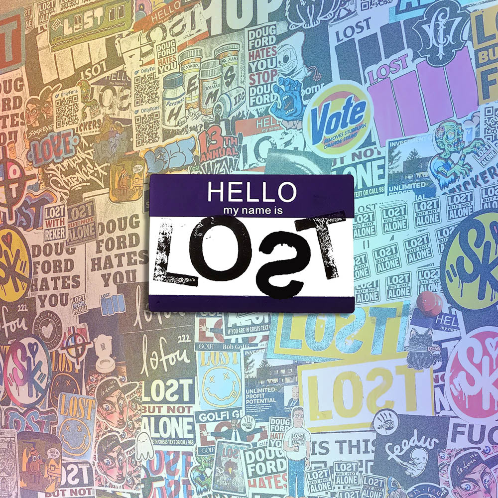 Hello my name is LOST sticker. A purple and white nametag sticker stamped with the name LOST with a backwards S. The sticker is set against a wall of stickers from international graffiti artists.